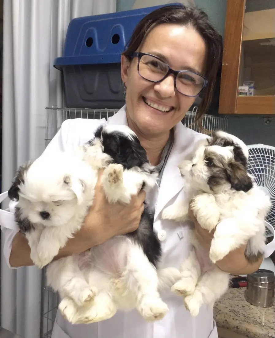 Veterinária de jaleco sorrindo com dois filhotes no colo, dentro da clínica