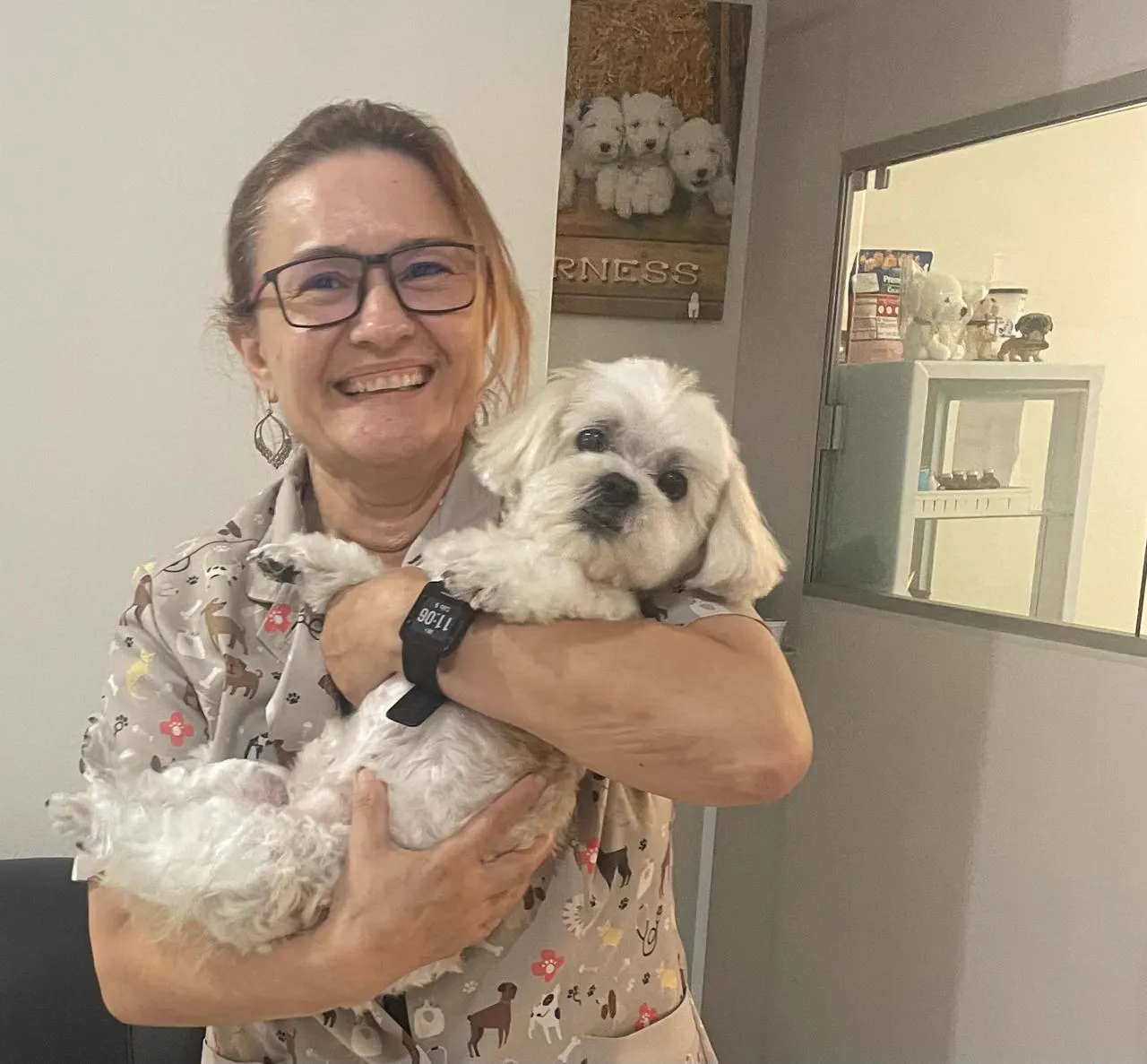 Dra. Valdette Carvalho sorrindo com um cachorrinho branco no colo, dentro da clínica